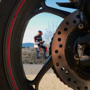 motard assis sur un muret à travers la roue de la moto