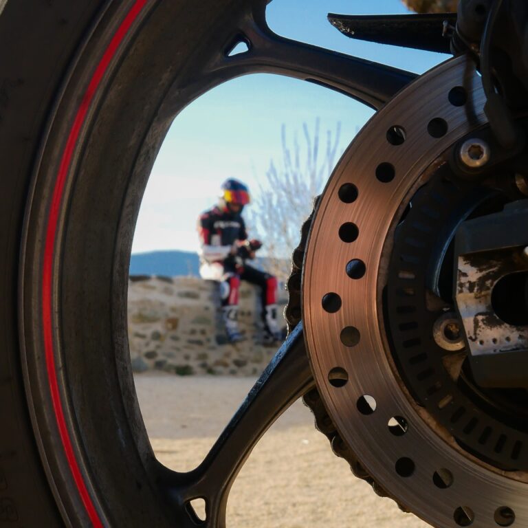 motard assis sur un muret à travers la roue de la moto